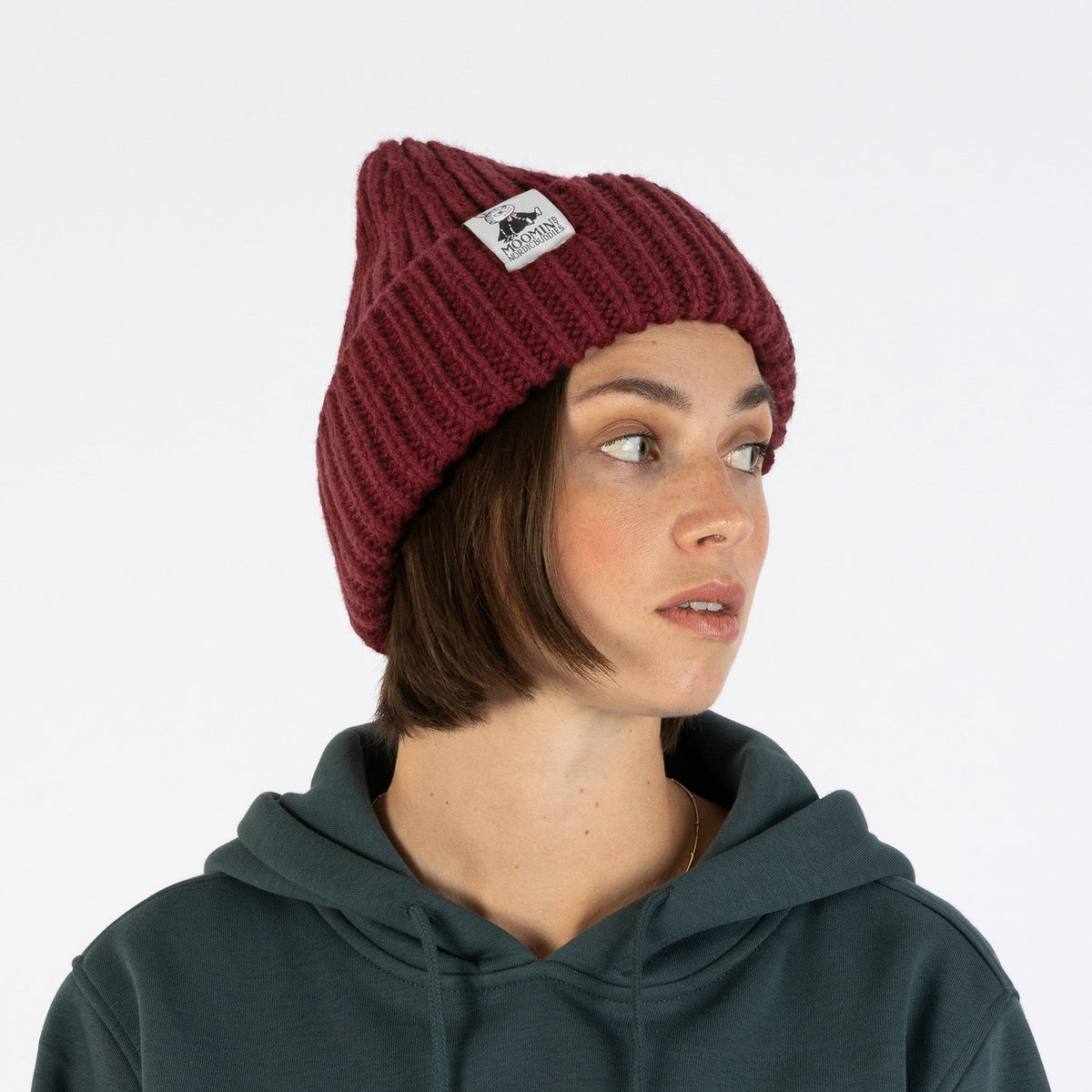 2. Woman in burgundy chunky beanie by Moomin NordicBuddies, side profile, with green hoodie, studio background