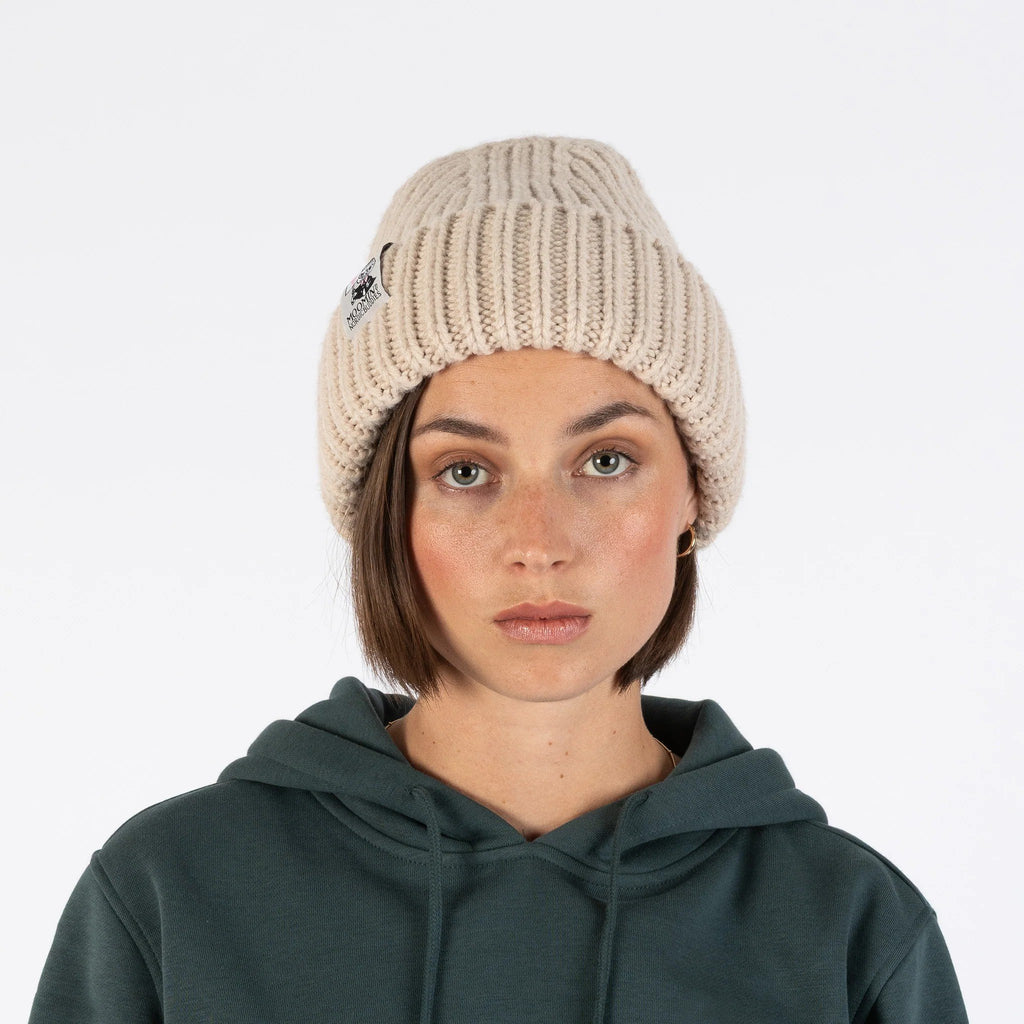 1. Woman wearing beige chunky beanie by Moomin NordicBuddies with green hoodie in studio setting