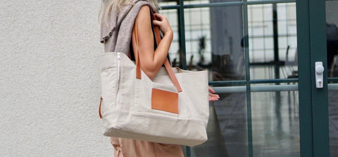 1. Woman carrying beige Liiva dog carrier and personal bag with brown leather accents, walking in urban setting