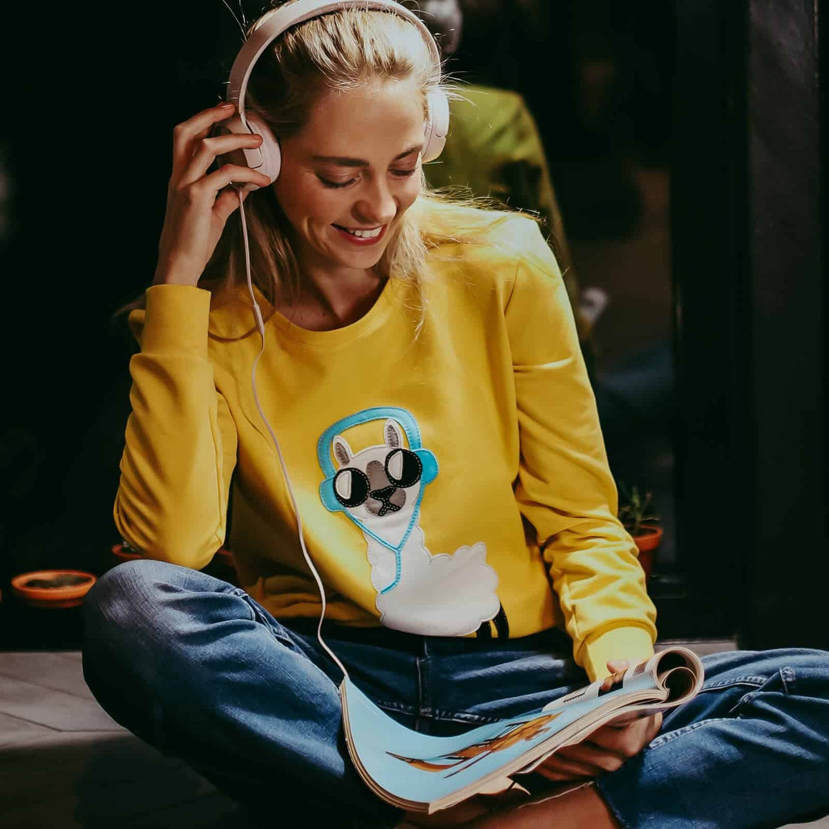 1. Women's yellow No Drama Llama sweatshirt by HILP, worn by model with headphones, in a cozy lifestyle setting
