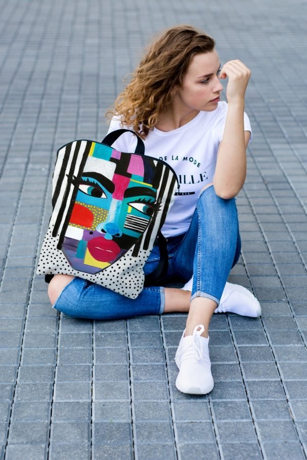 2. Woman sitting on pavement with Garbanota BACKPACK LOLITA featuring vibrant artistic design