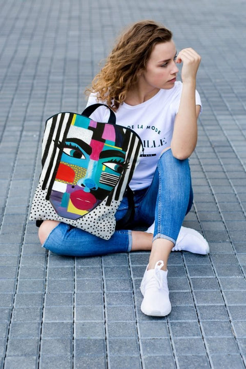 2. Woman sitting on pavement with Garbanota BACKPACK LOLITA featuring vibrant artistic design