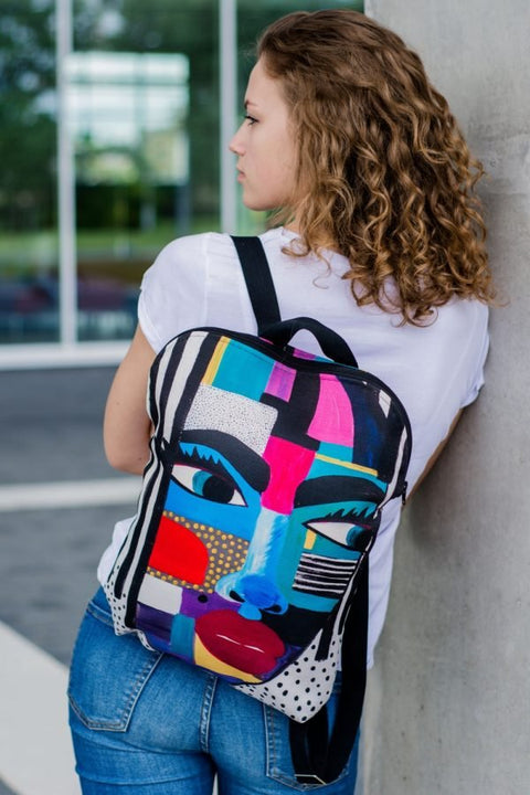 1. Woman wearing Garbanota BACKPACK LOLITA with colorful artwork by Dovilė Aleksonė, leaning against a wall