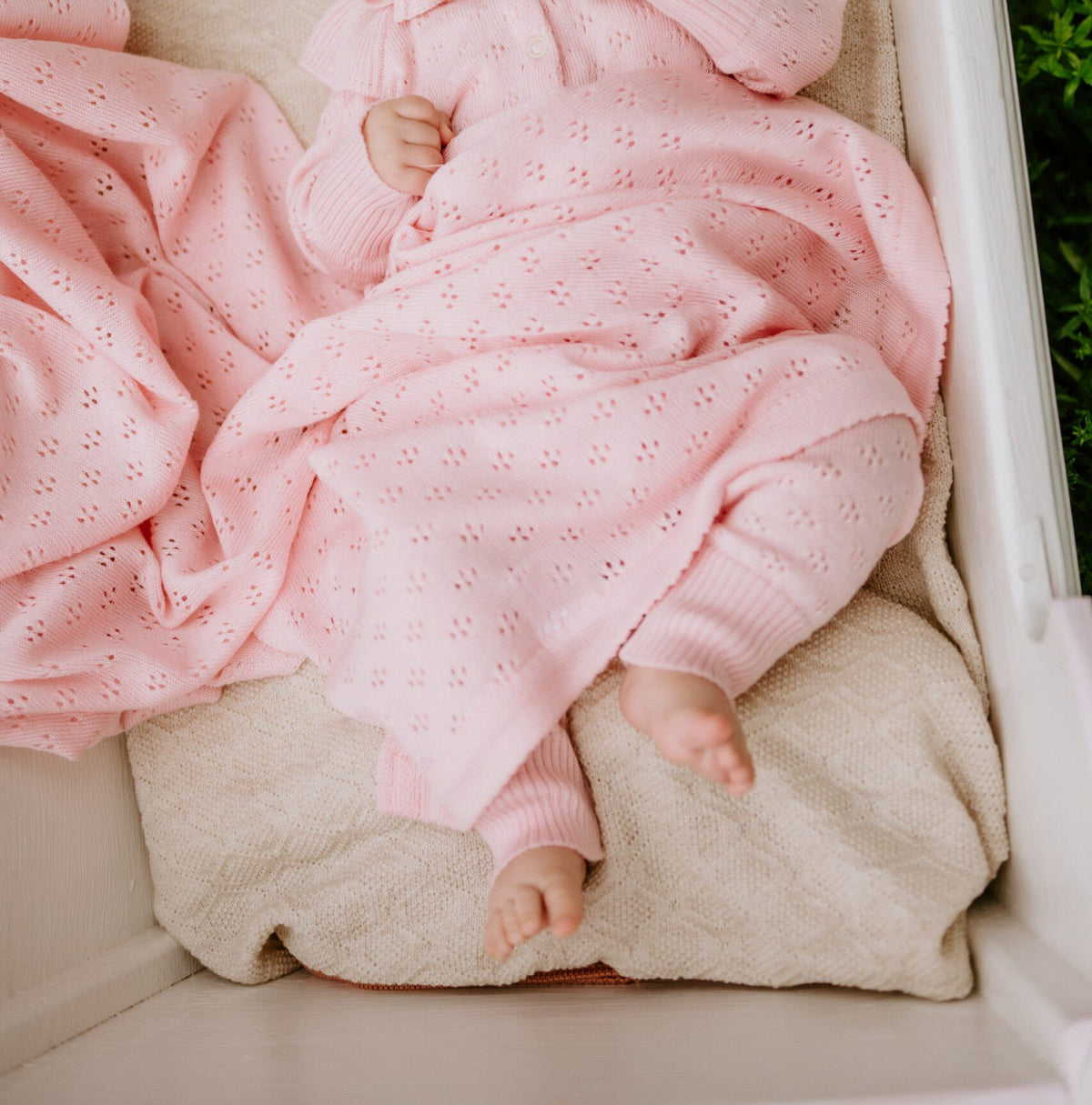 9. Baby's legs wrapped in pink merino wool blanket and bonnet in a cradle