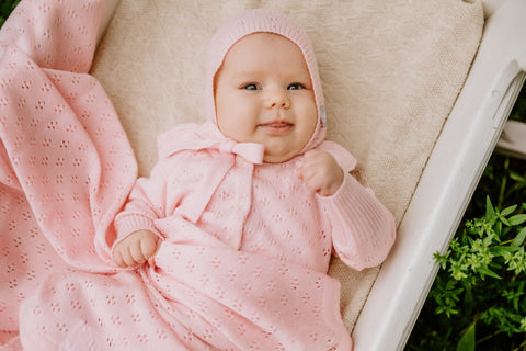 2. Smiling baby wrapped in pink merino wool blanket and bonnet lying on a soft surface outdoors