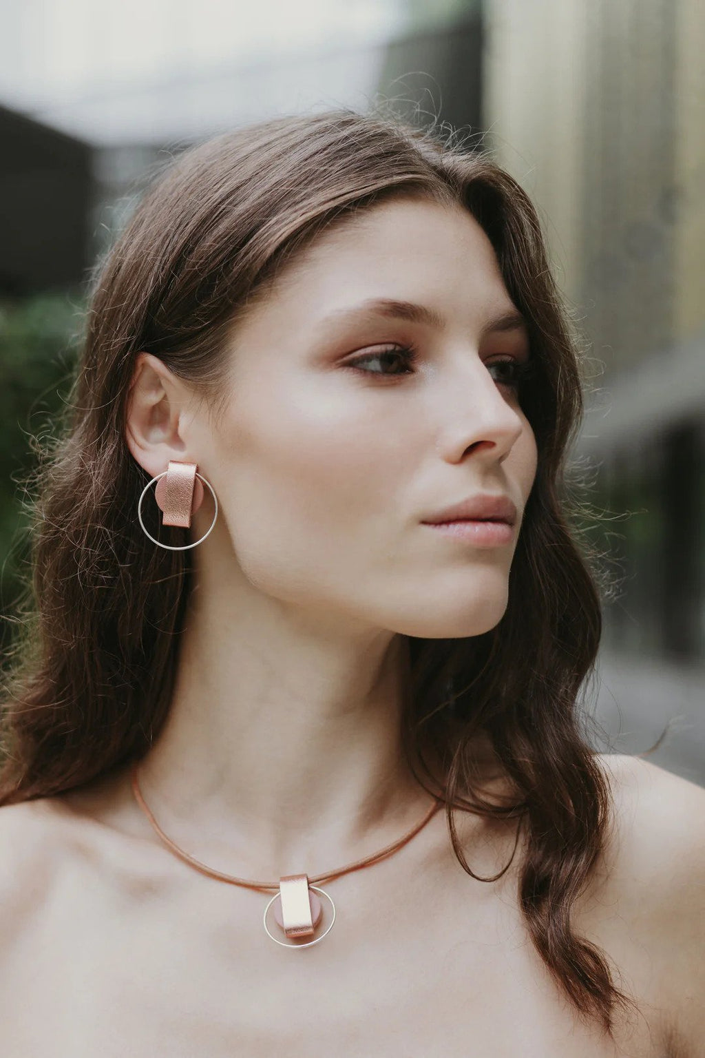 1. Woman wearing Gerda Retter Design Luce Mini Handmade Necklace in caramel brown, showcasing geometric pendant and matching earrings in lifestyle setting