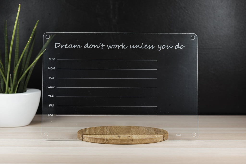 1. Clear acrylic school planner with motivational quote 'Dream don't work unless you do' on wooden stand, placed on light wood surface with plant in background