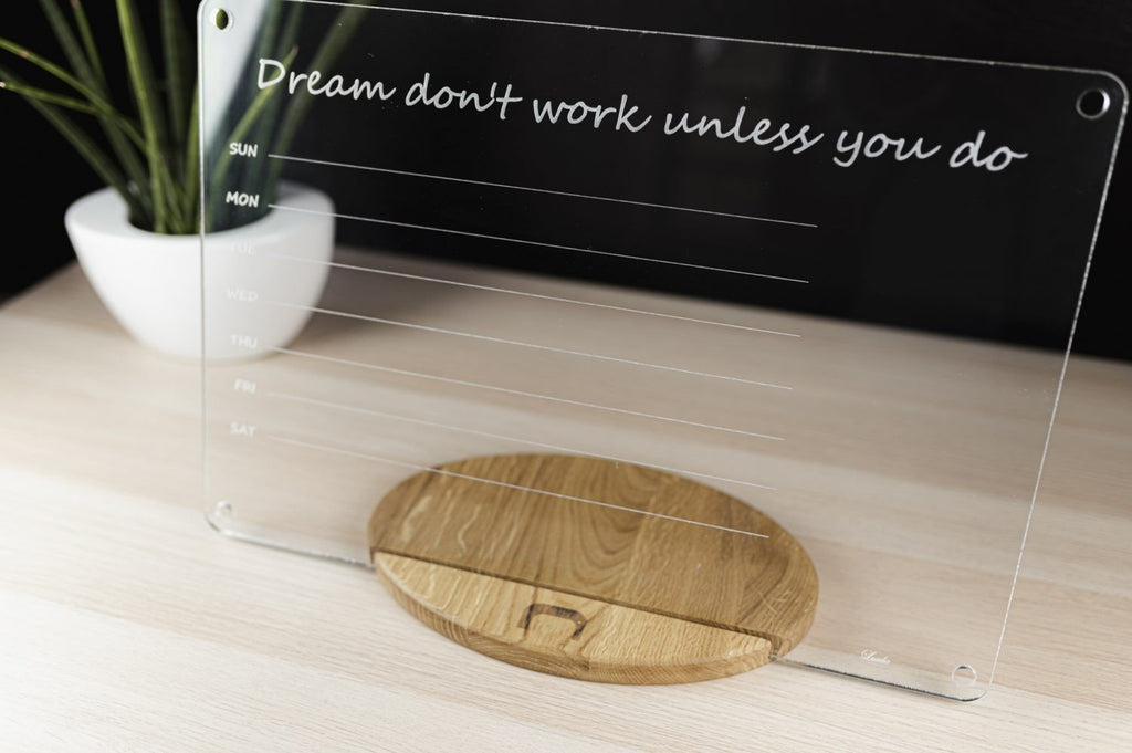 6. Clear acrylic planner with quote 'Dream don't work unless you do' on wooden stand, showing weekly layout on light wood surface