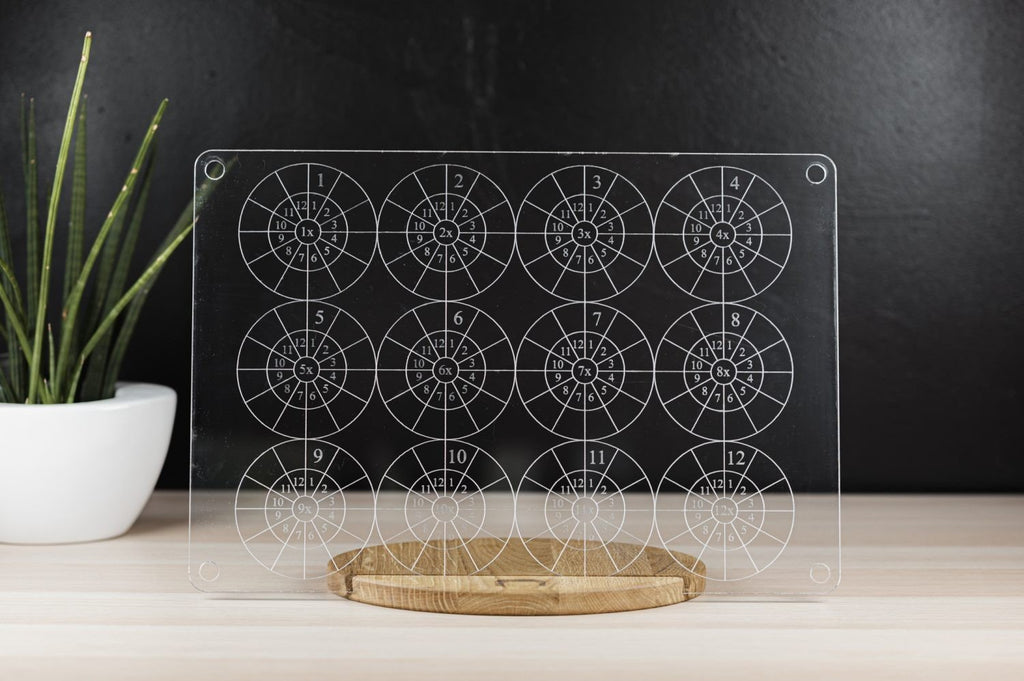 1. LUULA multiplication wall board on wooden stand with plant in background, featuring laser-engraved multiplication tables on clear acrylic