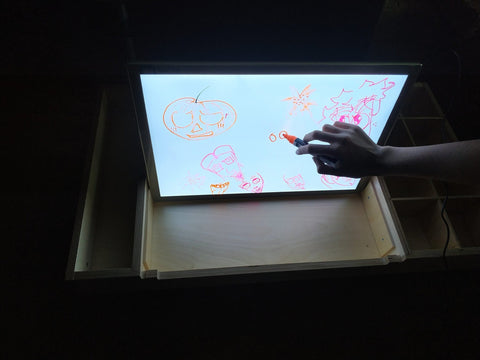 1. Child drawing on Luula light board with colorful markers in a dark room