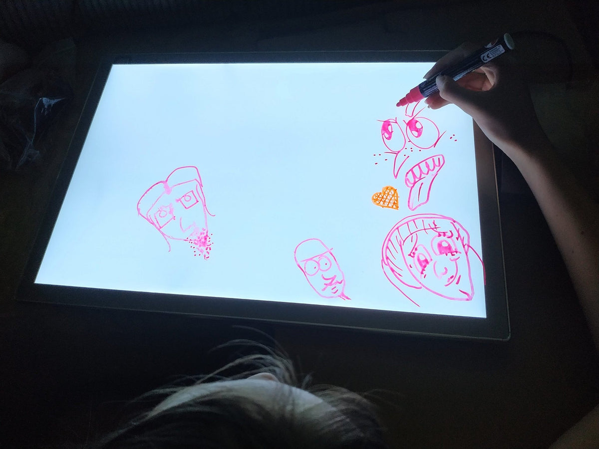 1. Child using Luula light board to draw faces with red marker in a dark room