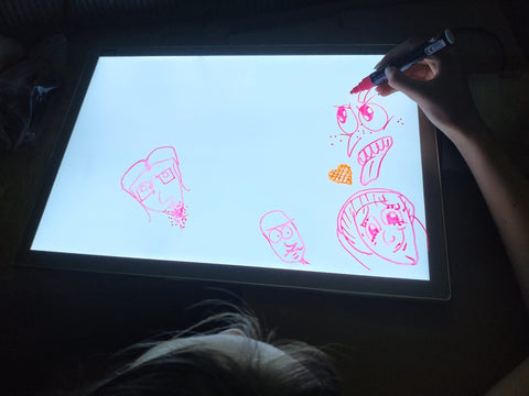 1. Child using Luula light board to draw faces with red marker in a dark room