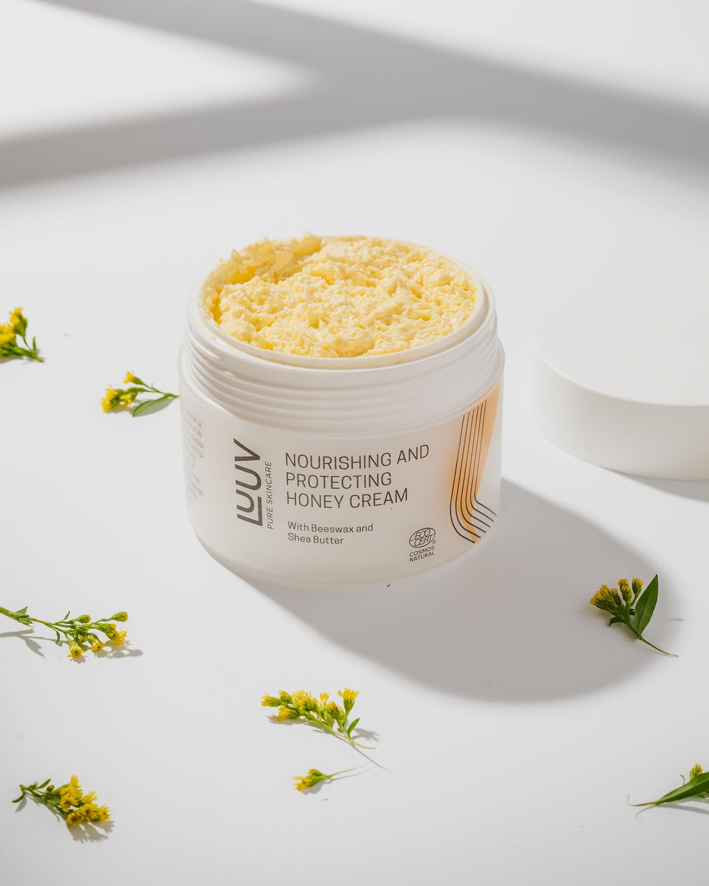 5. LUUV Nourishing and Protecting Honey Cream with open lid, highlighting creamy texture, styled with yellow flowers