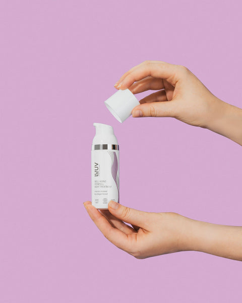 3. Hands holding LUUV Well-aging Stemcell Night Treatment bottle with cap removed, against a pink background