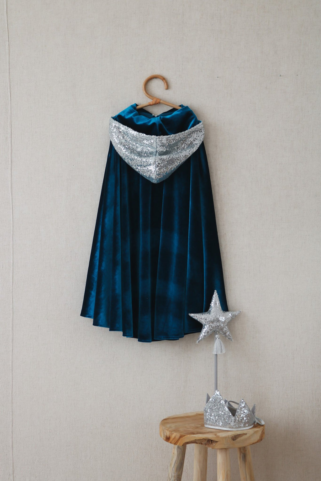 6. Blue velour cape with silver hood hanging on wall with star wand and crown on stool