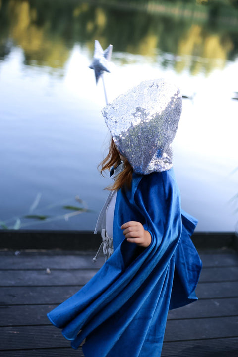 2. Child in blue cape with silver hood holding star wand by a lake