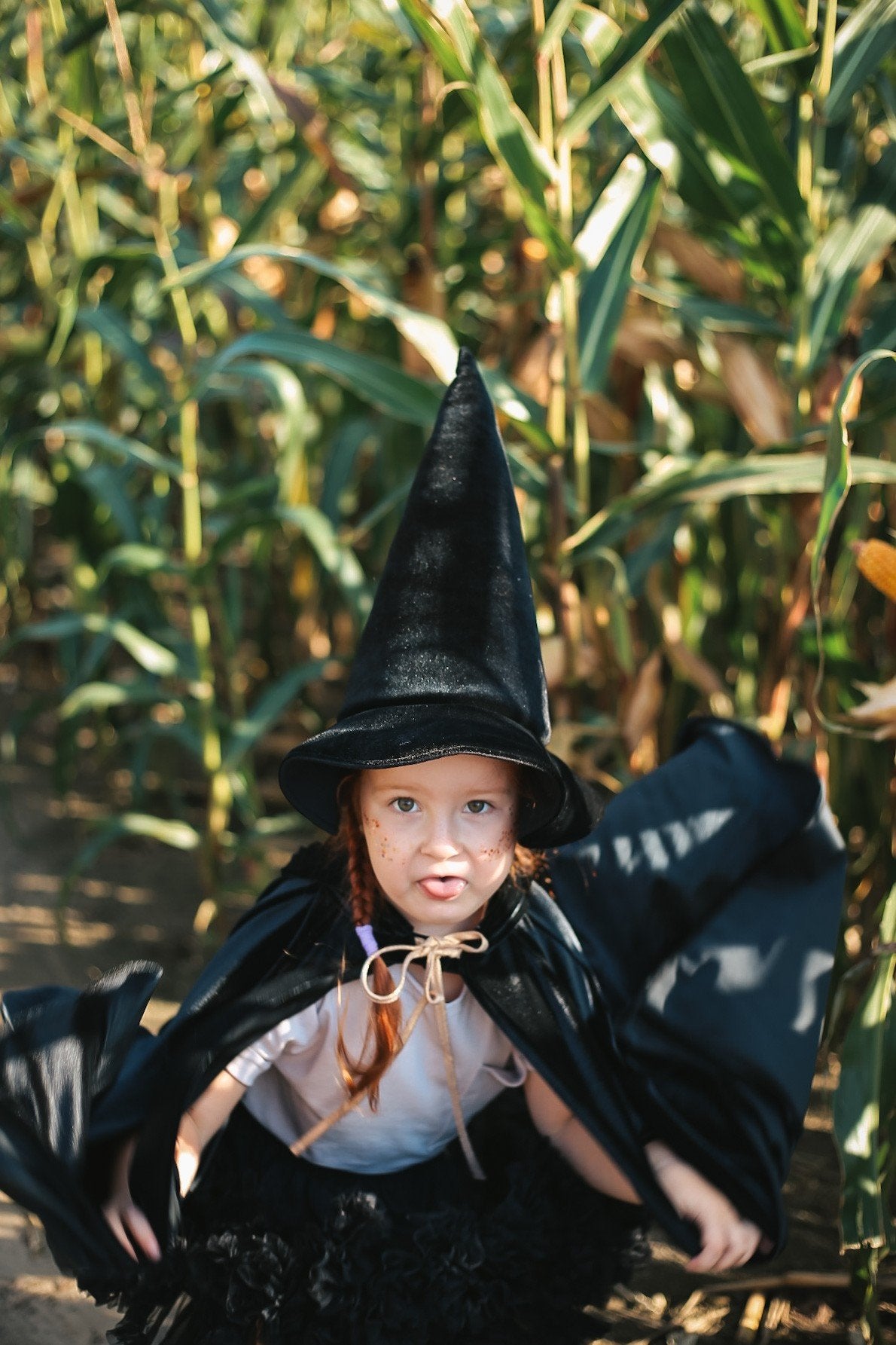6. Child in black cape and witch hat in a cornfield, smiling