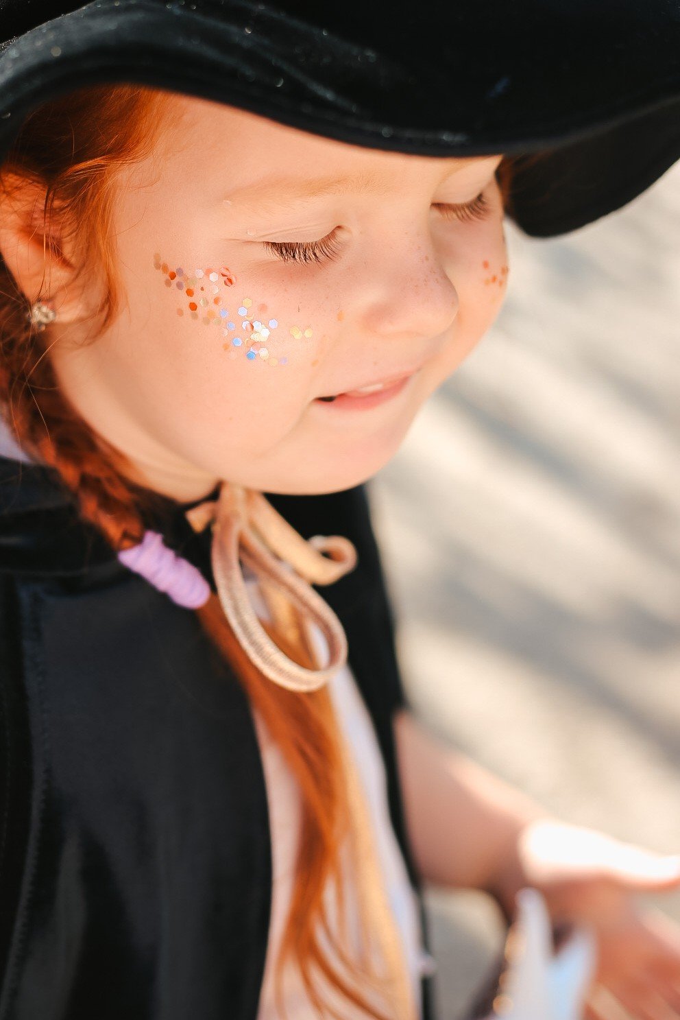 11. Close-up of child in black cape with glitter on face outdoors