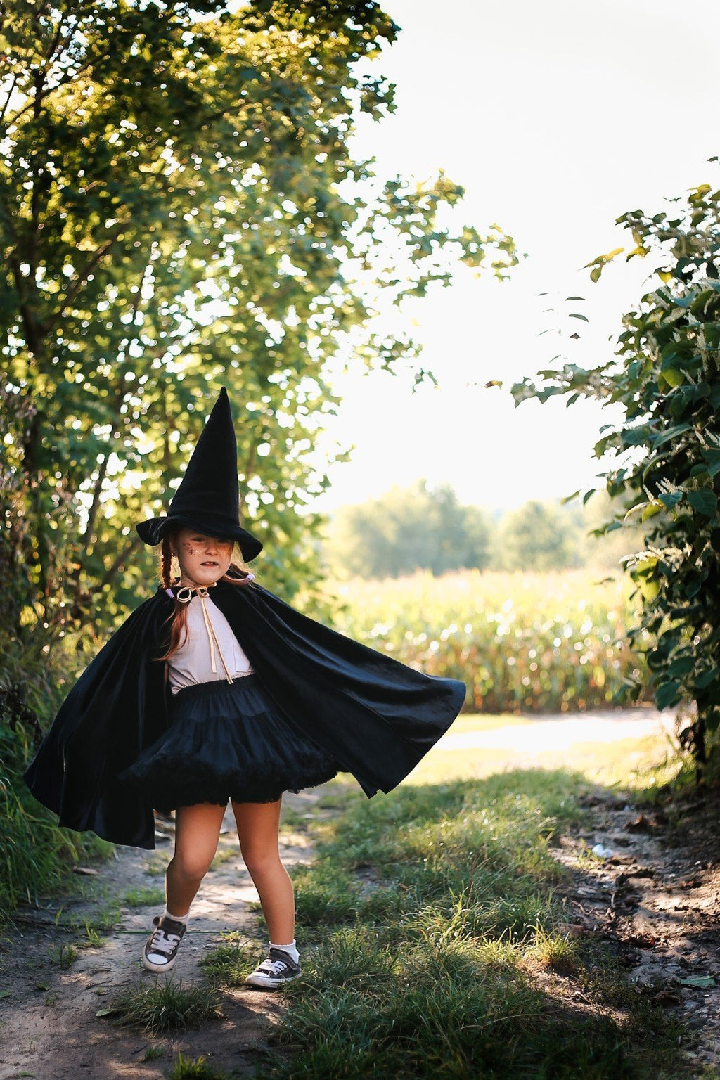 9. Child in black cape and witch hat walking on a path in a sunny outdoor setting