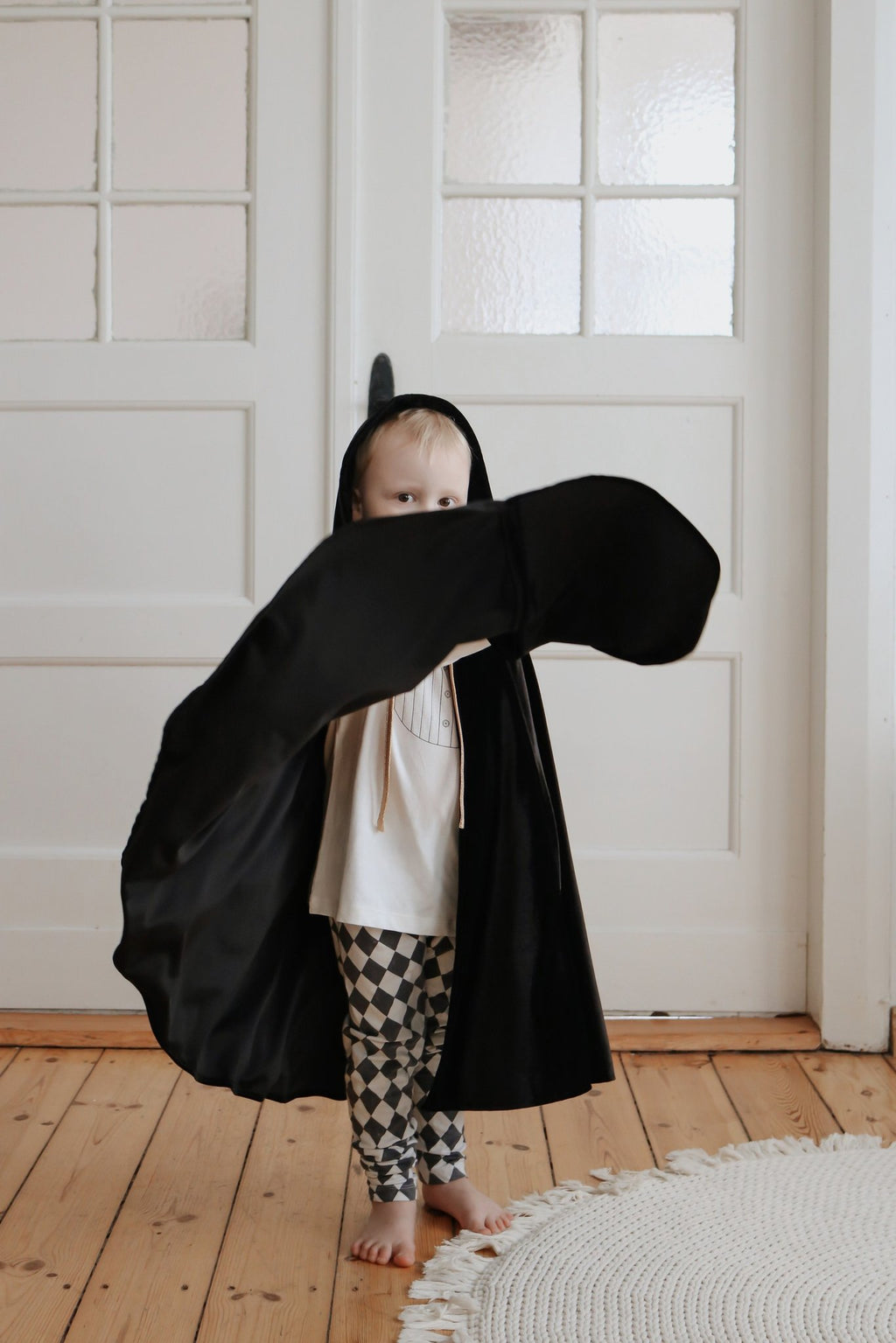 5. Child in black cape with hood playing indoors, showing cape's movement