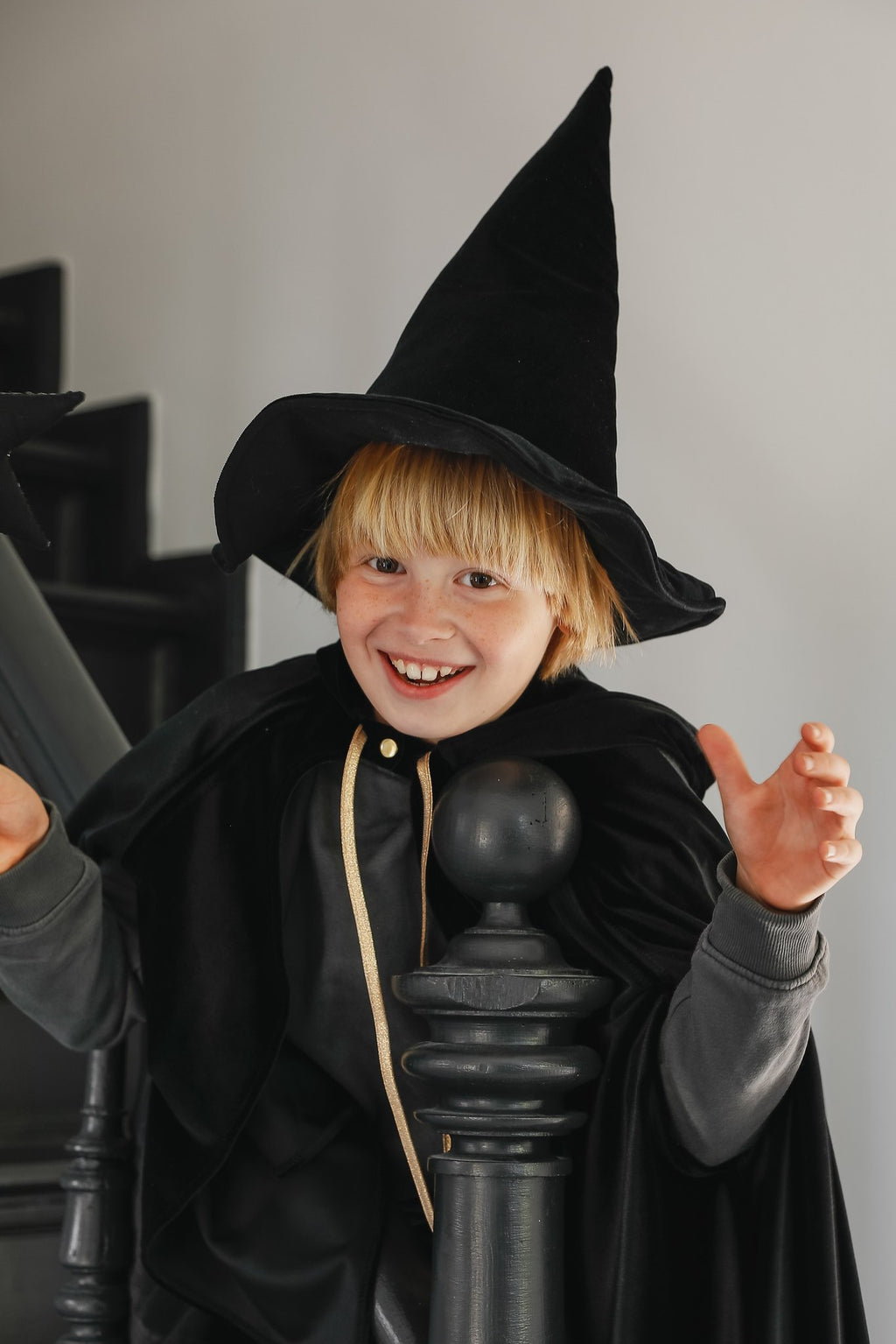 14. Child in black cape and witch hat making a playful gesture on stairs