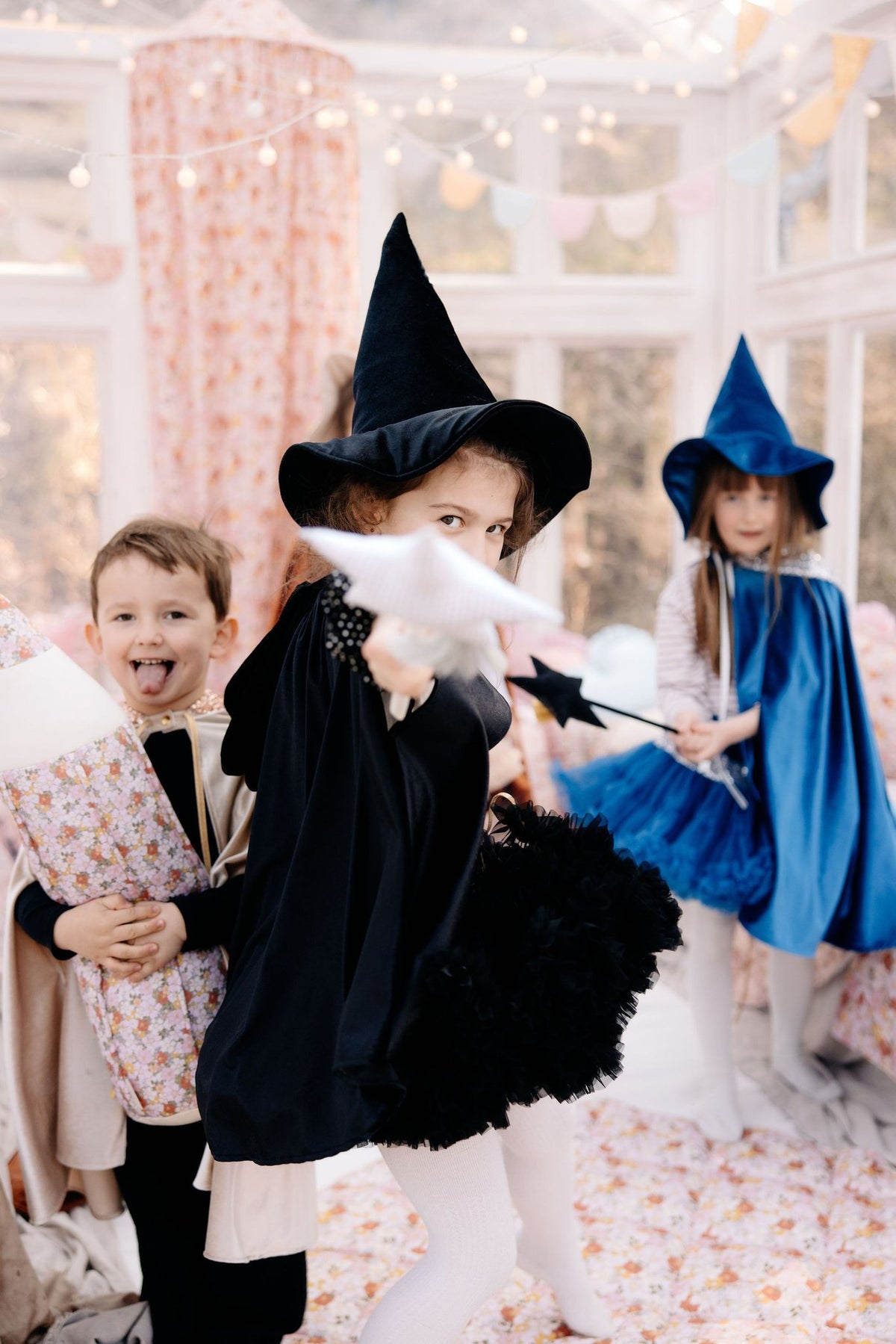 17. Three children in fantasy costumes, one in black cape, playing with wands in a decorated room