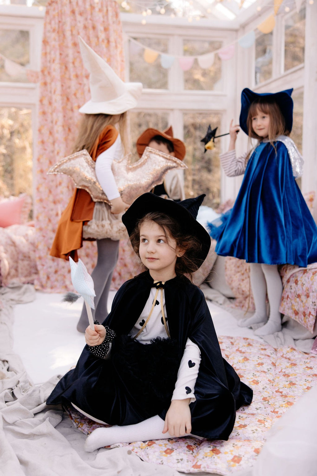 2. Three children in fantasy costumes, one in black cape, playing in a decorated room