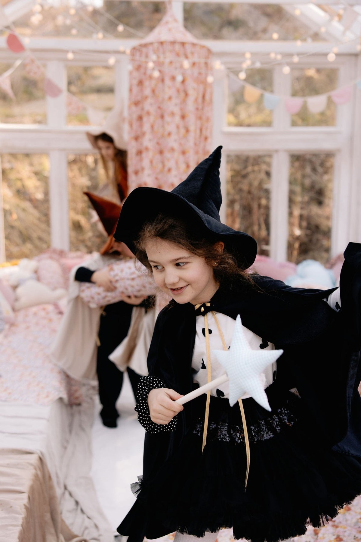 16. Child in black cape and witch hat holding a star wand in a decorated room