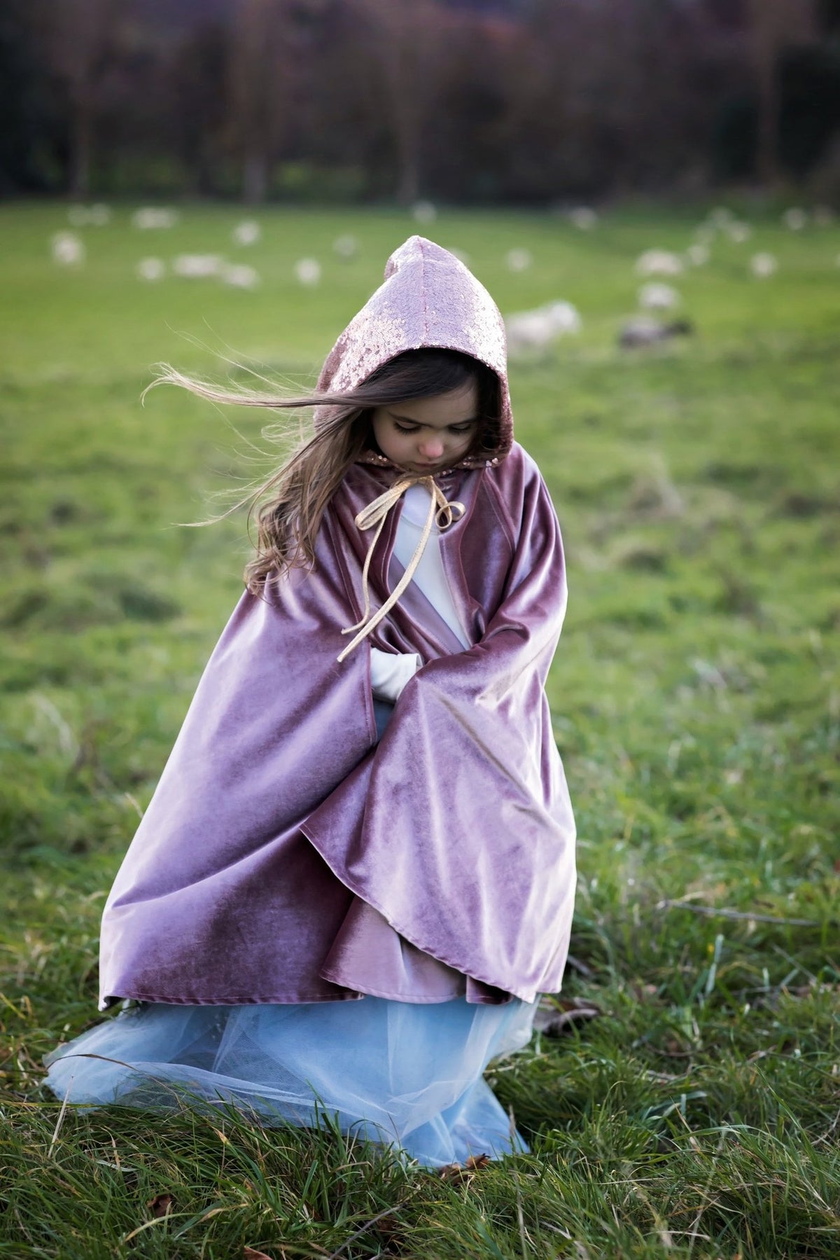 1. Girl wearing cosmic pearl cape with hood in a grassy field, showcasing the velour fabric and magical design