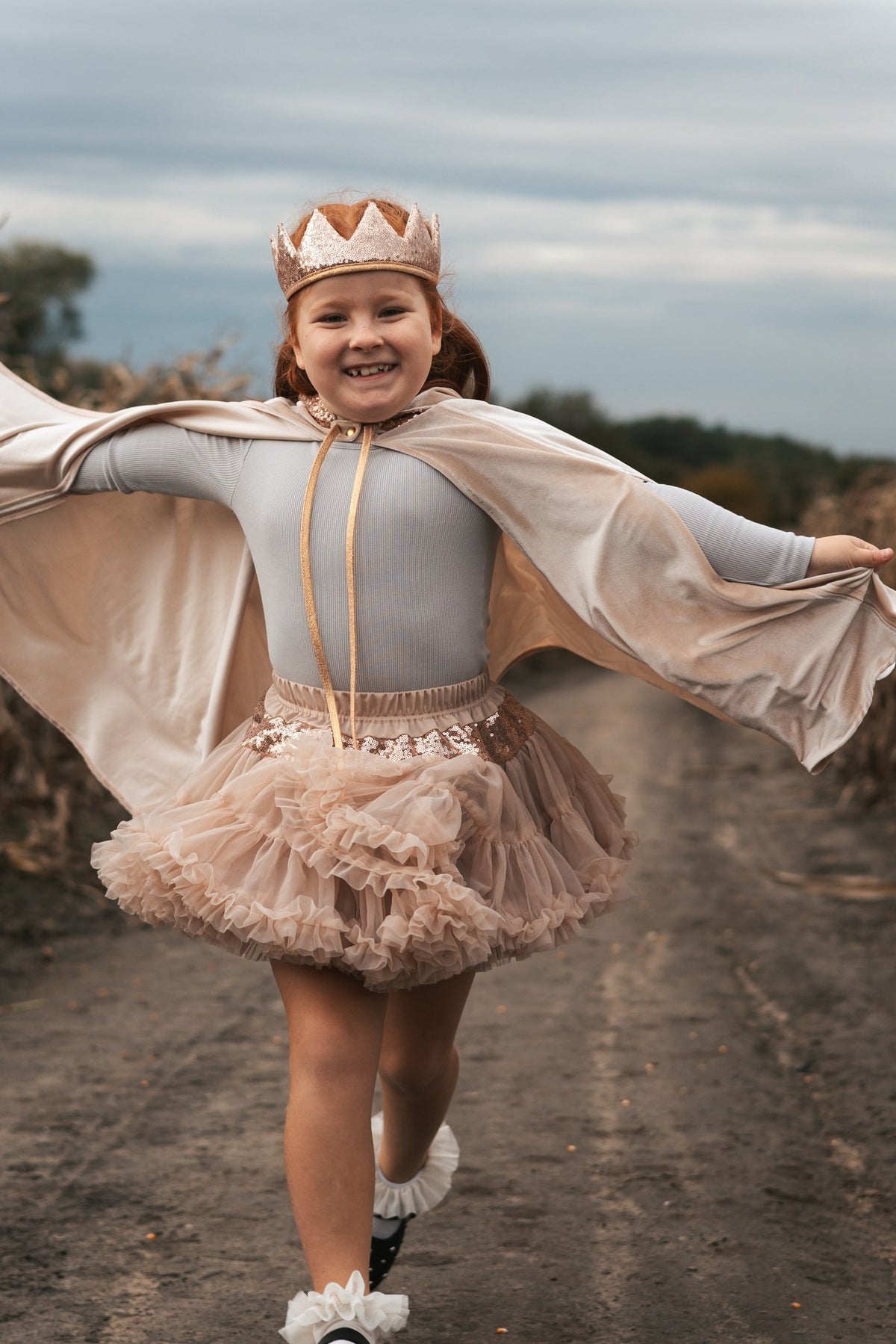 2. Smiling girl in cream cape and crown running on dirt path
