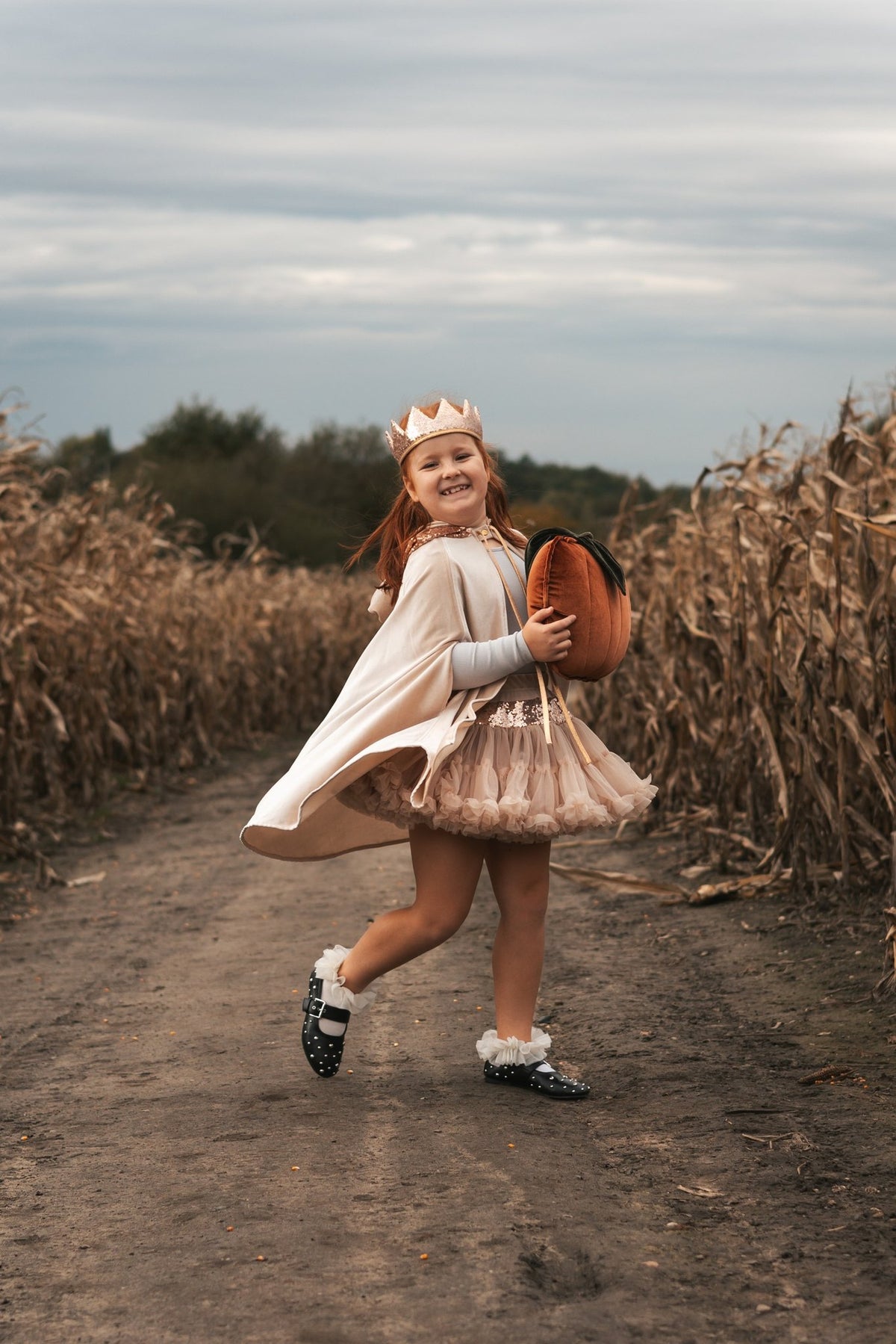 1. Girl wearing cream pearl cape and crown holding pumpkin in cornfield