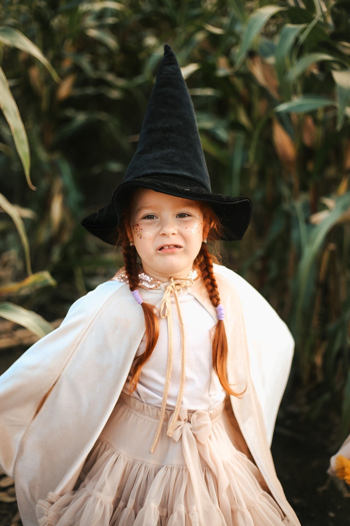 7. Girl in cream cape and black witch hat standing in cornfield