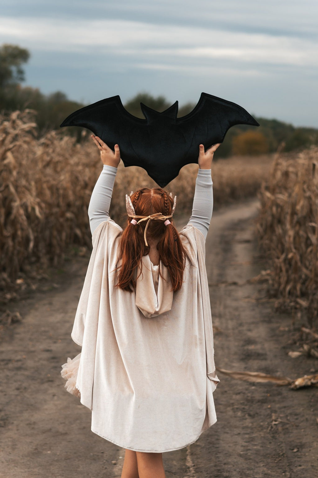 8. Girl in cream cape holding bat silhouette above head in field