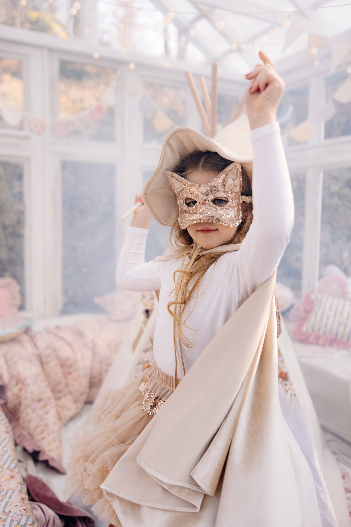 3. Child in cream cape and mask posing indoors with raised arm