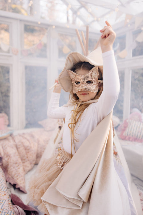 3. Child in cream cape and mask posing indoors with raised arm