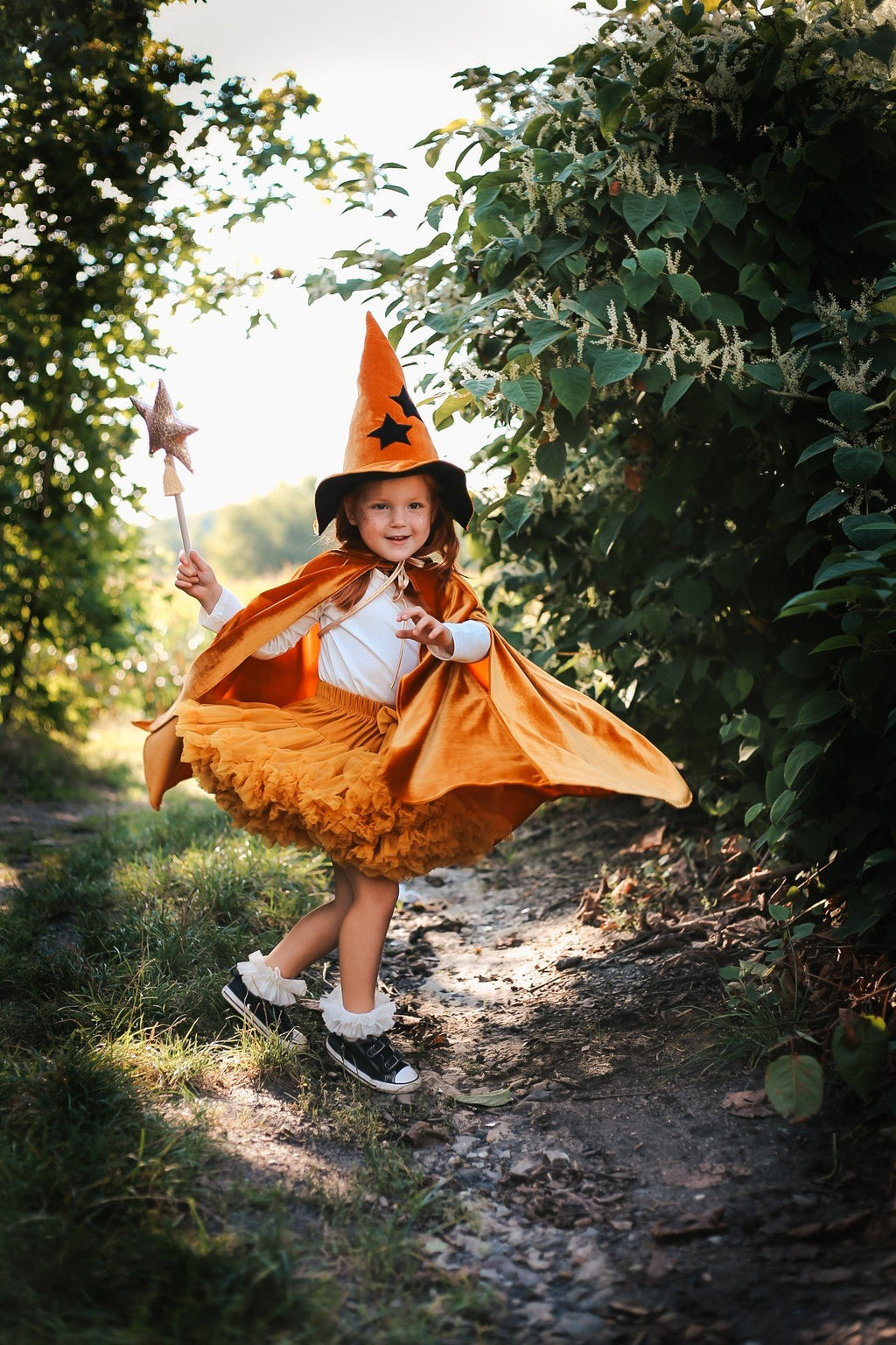 1. Child wearing golden cape and witch hat holding wand in forest path