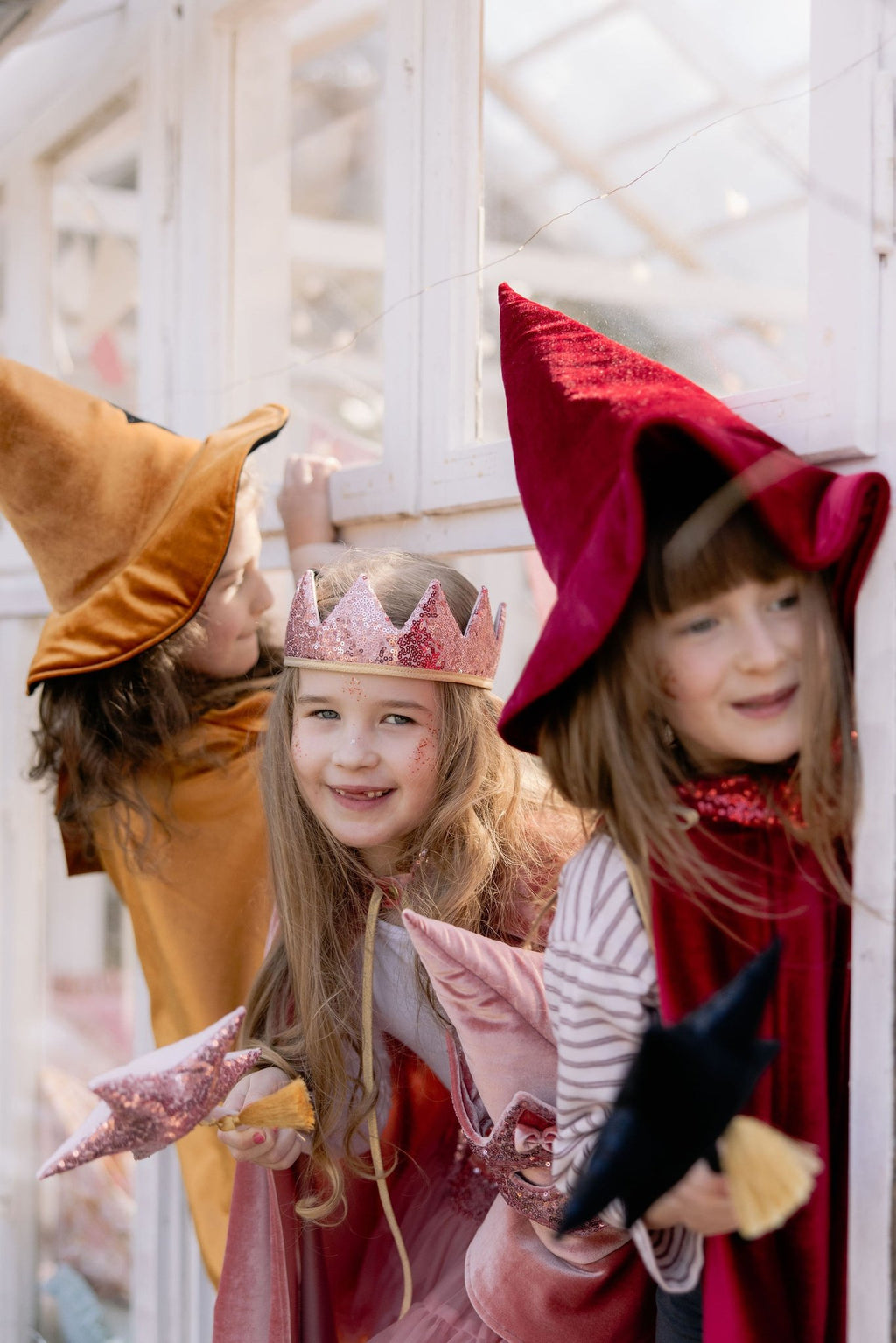 6. Three children in golden, red, and pink capes smiling indoors