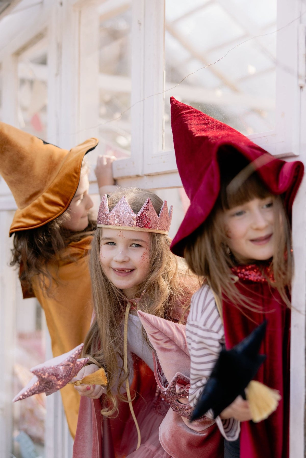 6. Three children in golden, red, and pink capes smiling indoors