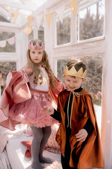 1. Two children in ginger and pink capes with crowns in a sunlit room, playing dress-up