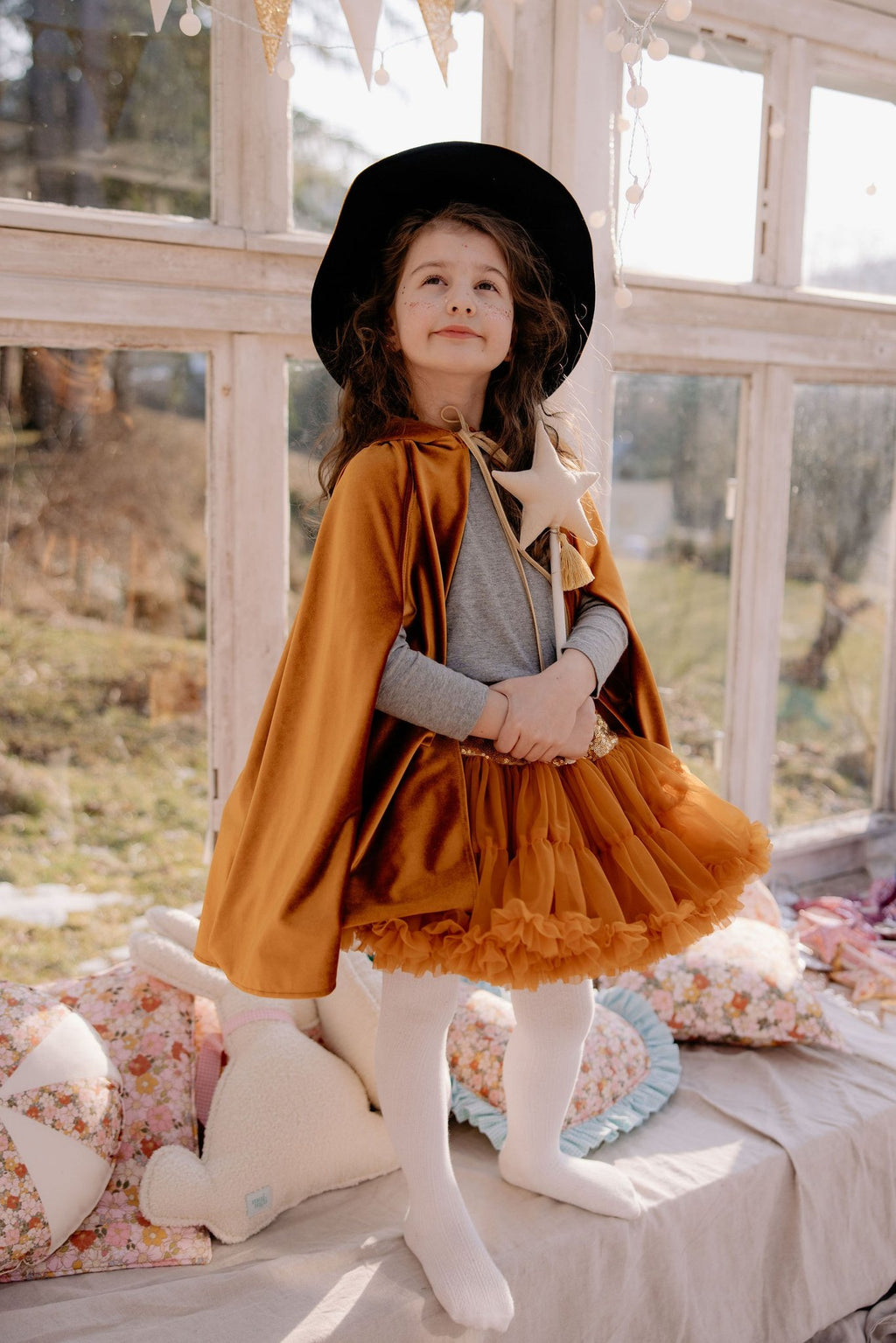 15. Child in golden cape and witch hat standing on cushions