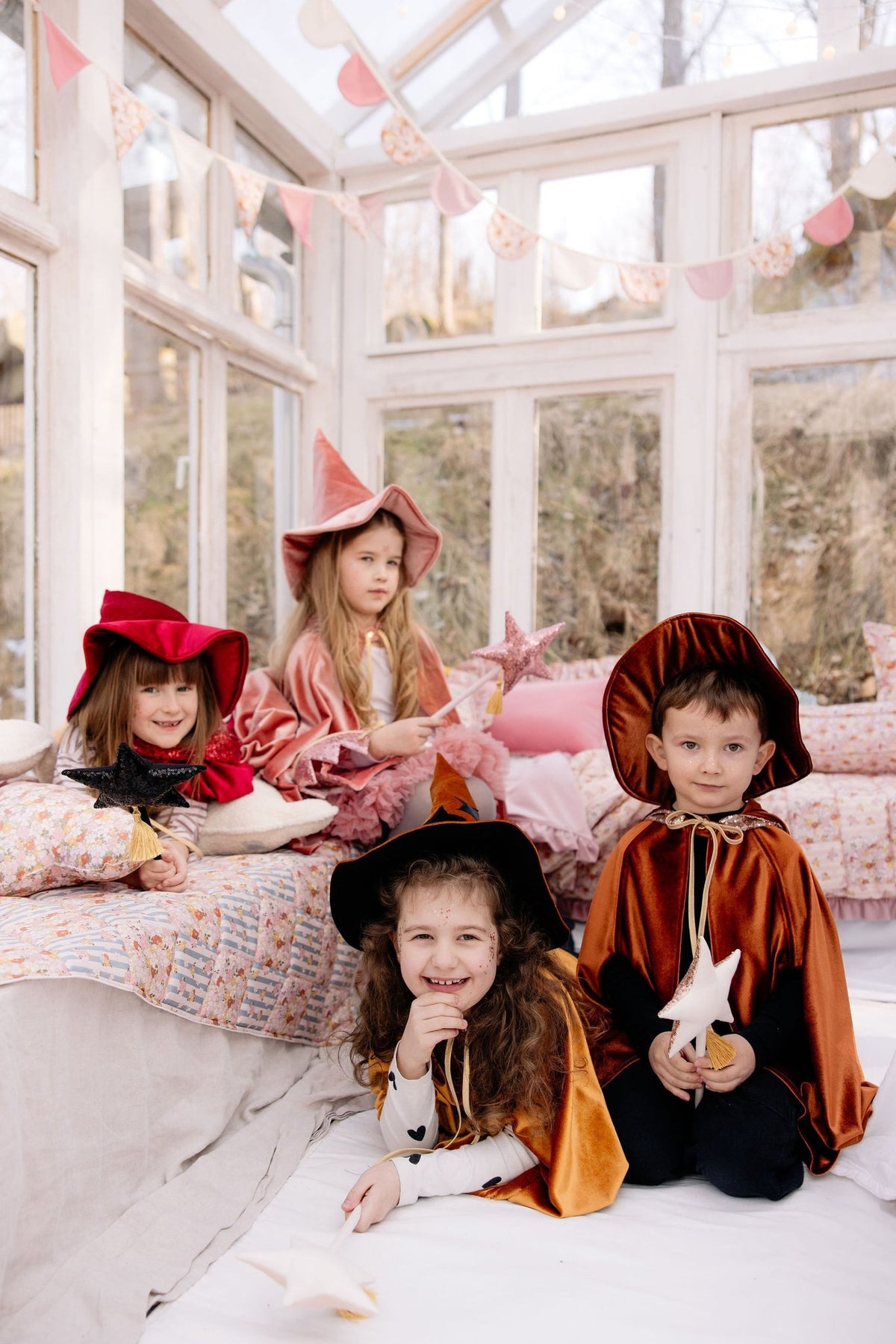1. Four children in colorful capes and hats posing on a bed in a sunlit room