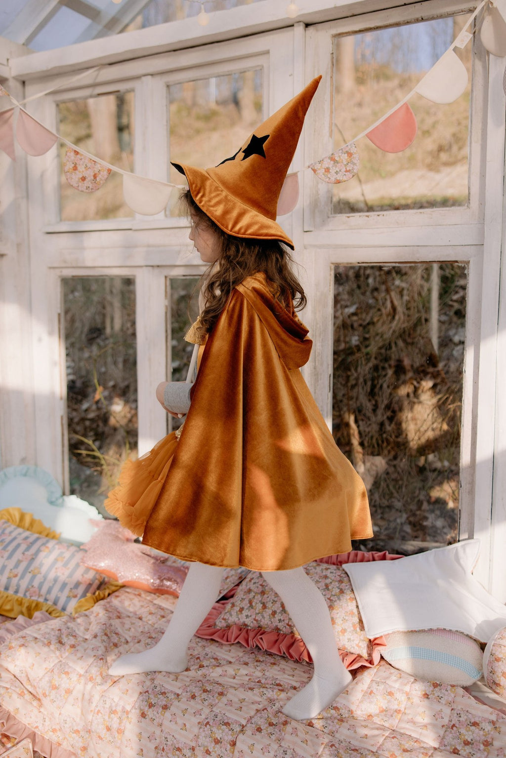 13. Child in golden cape and witch hat walking indoors