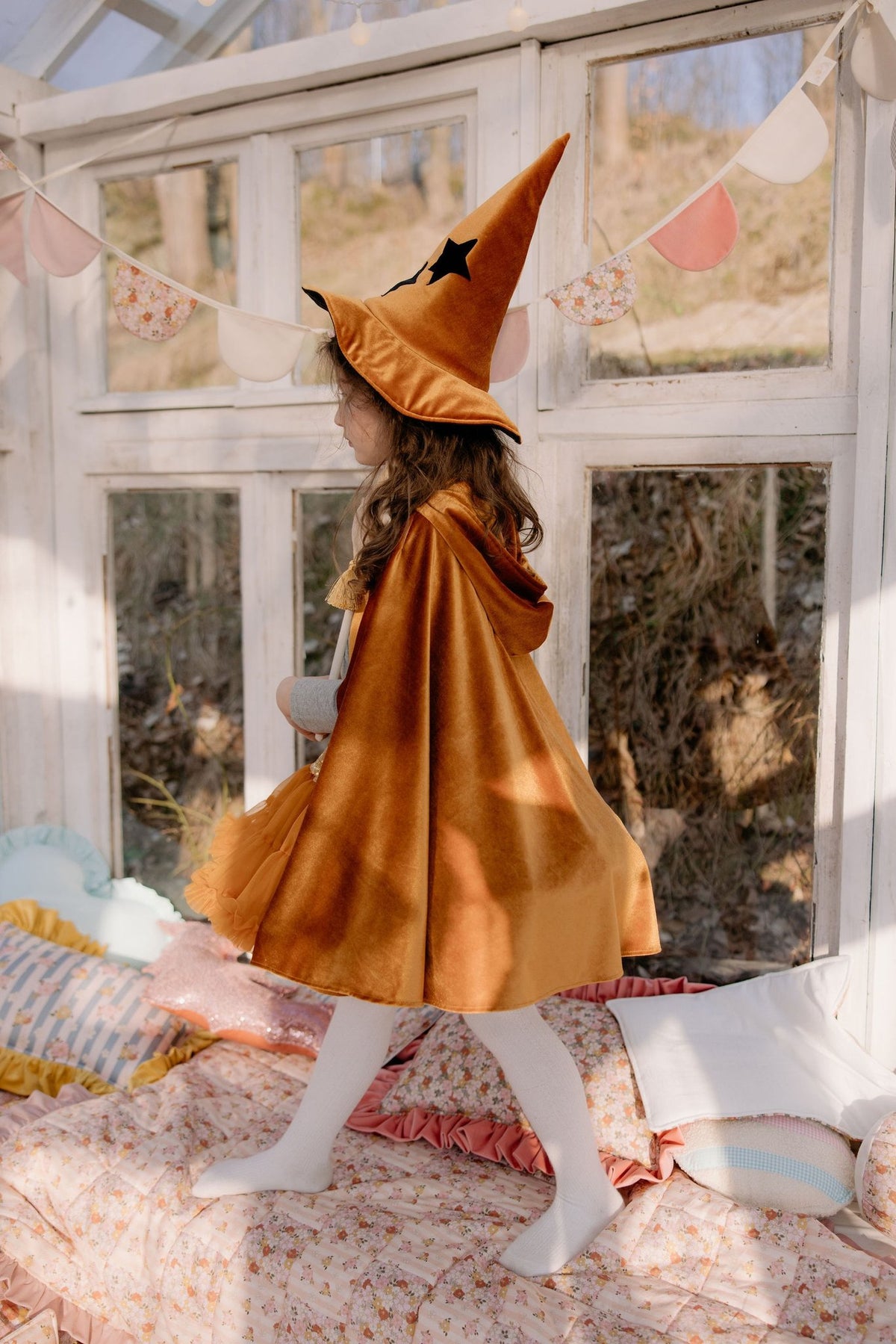 13. Child in golden cape and witch hat walking indoors