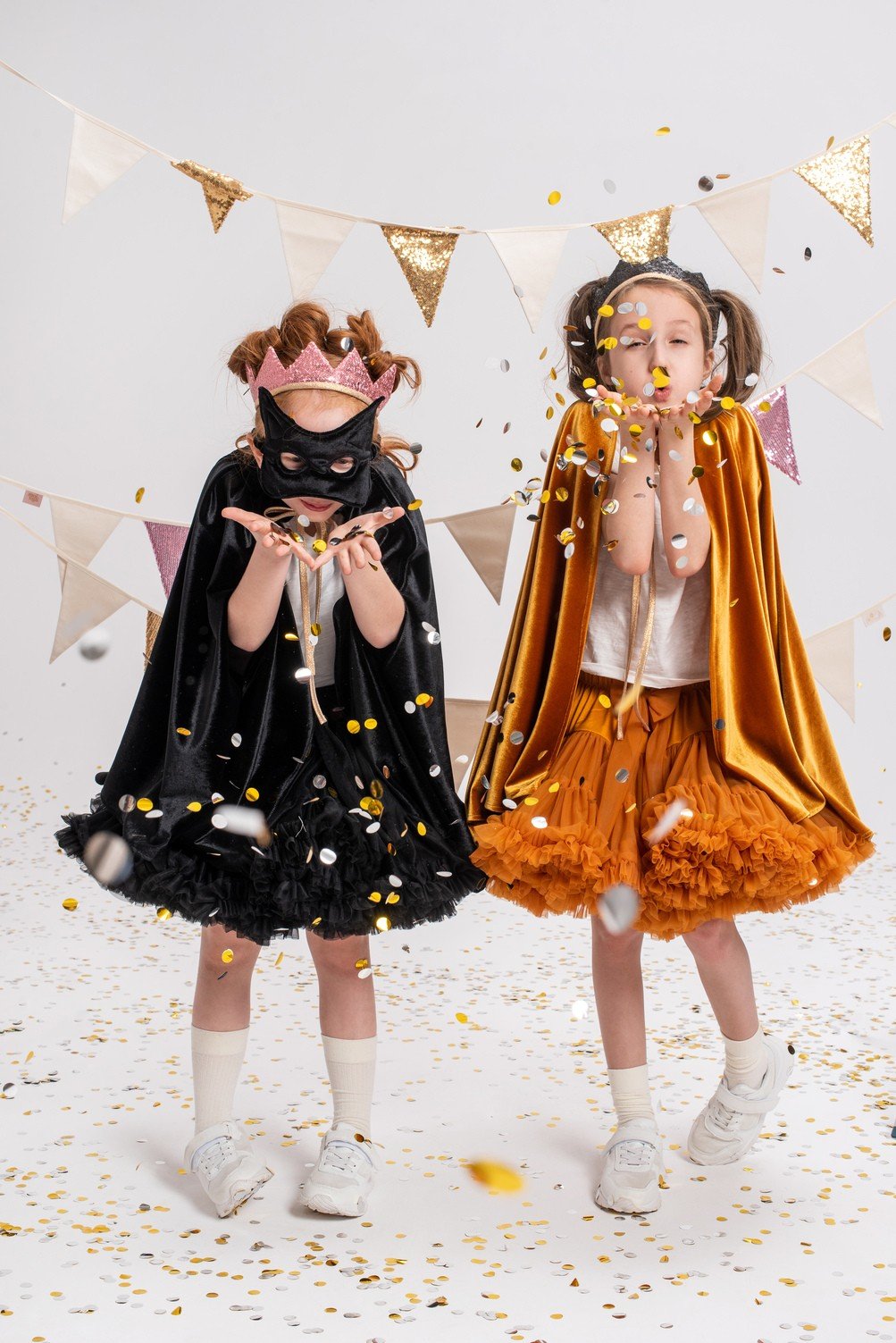 9. Two children in golden and black capes with confetti in studio