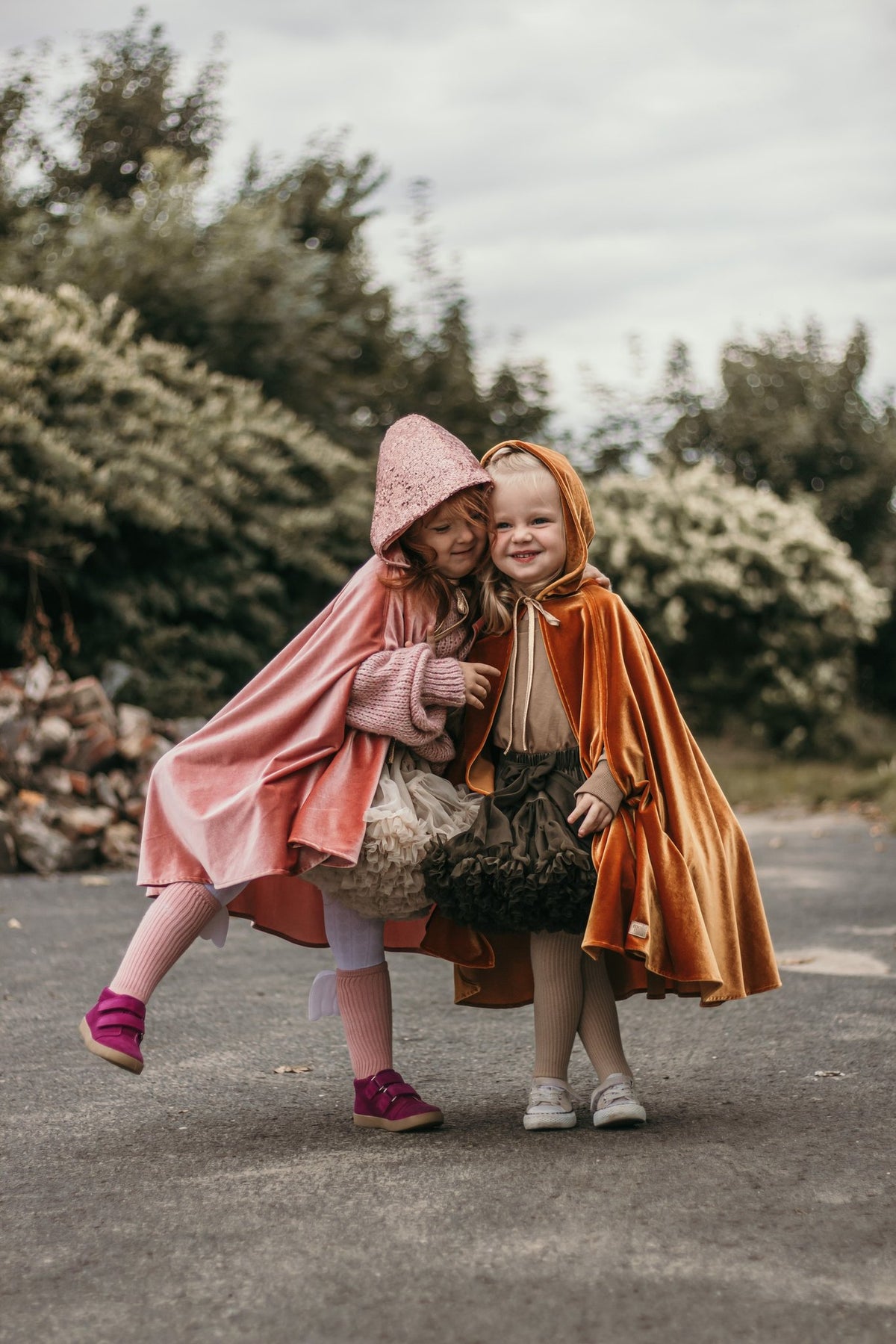 5. Two children in pink and orange capes hugging and smiling outdoors