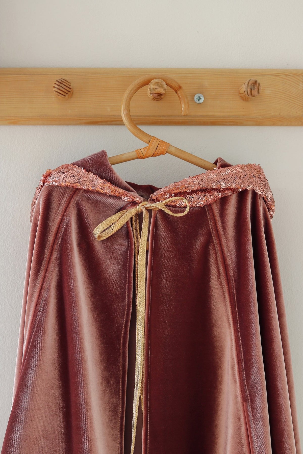 9. Close-up of pink velour cape with hood hanging on wooden hook