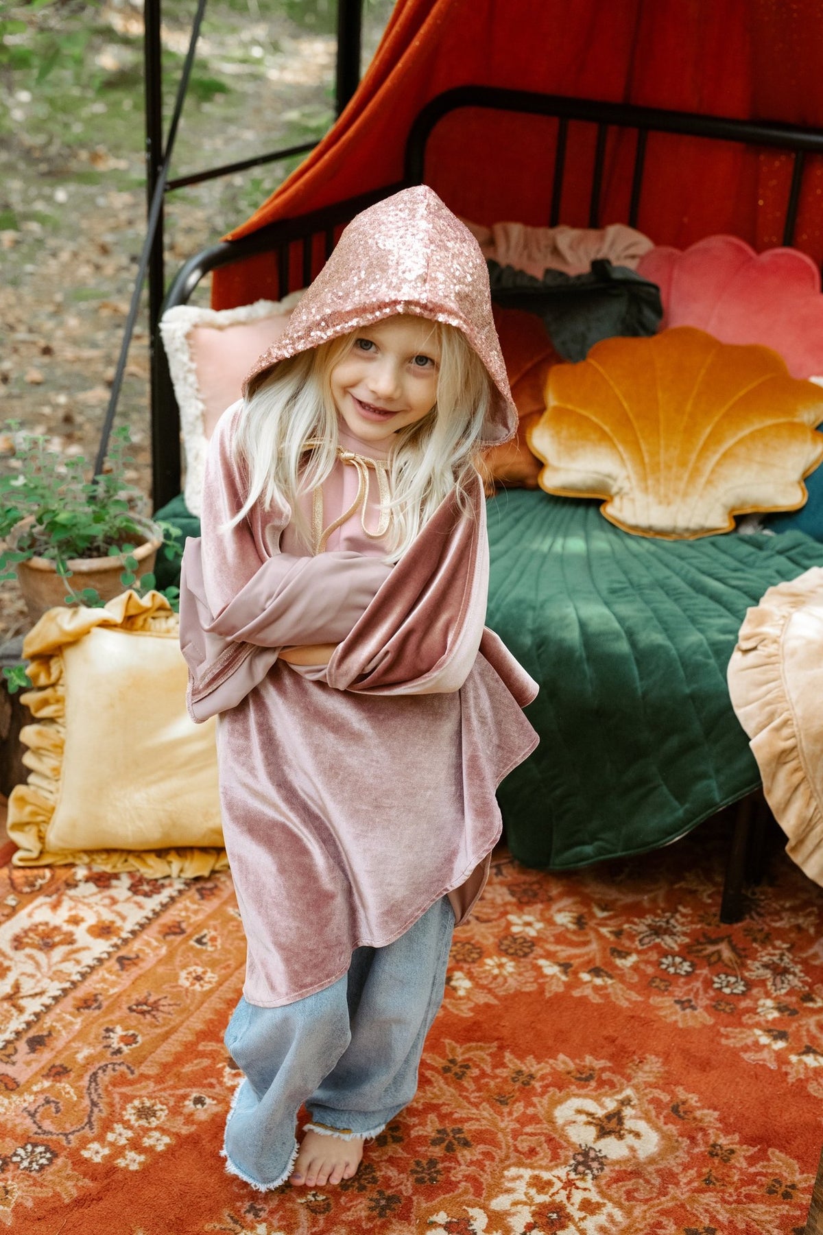 3. Child wearing a pink cape with hood smiling in a cozy room with colorful cushions