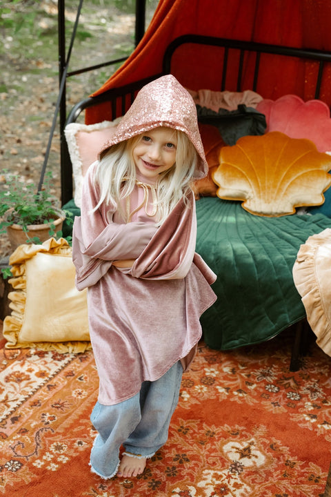 3. Child wearing a pink cape with hood smiling in a cozy room with colorful cushions