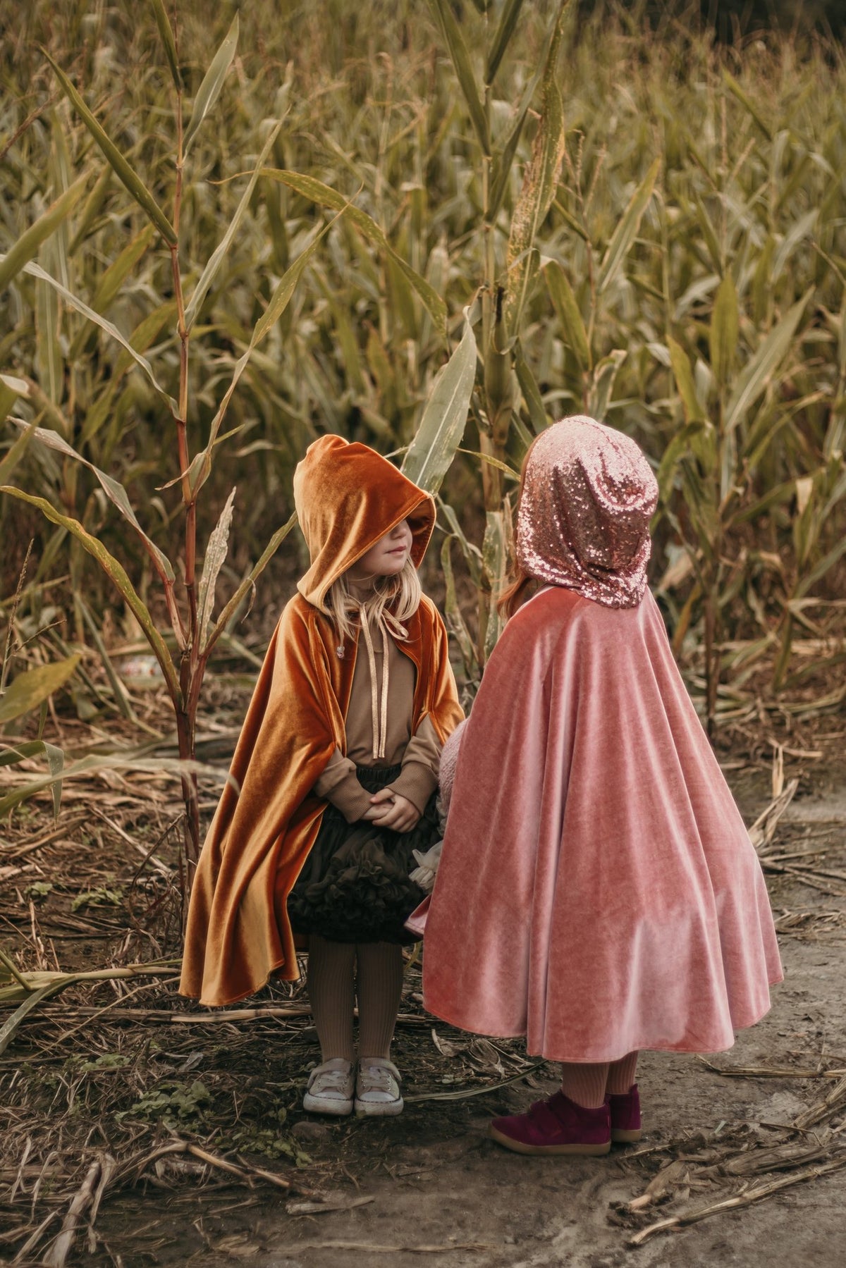 8. Two children in pink and orange capes facing each other in a cornfield