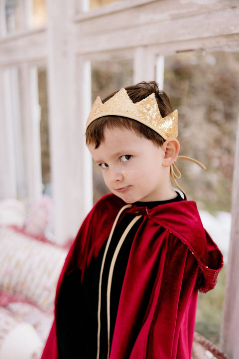 4. Close-up of boy in red velour cape and gold crown, standing in a room with large windows